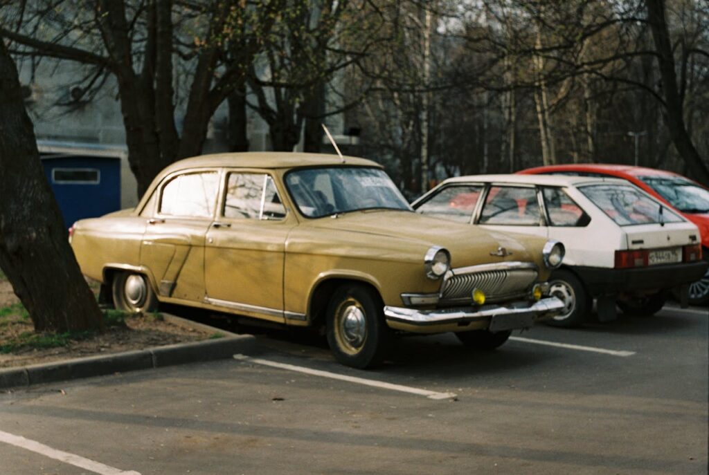 Classic vintage car parked outdoors in an urban parking lot with trees around.