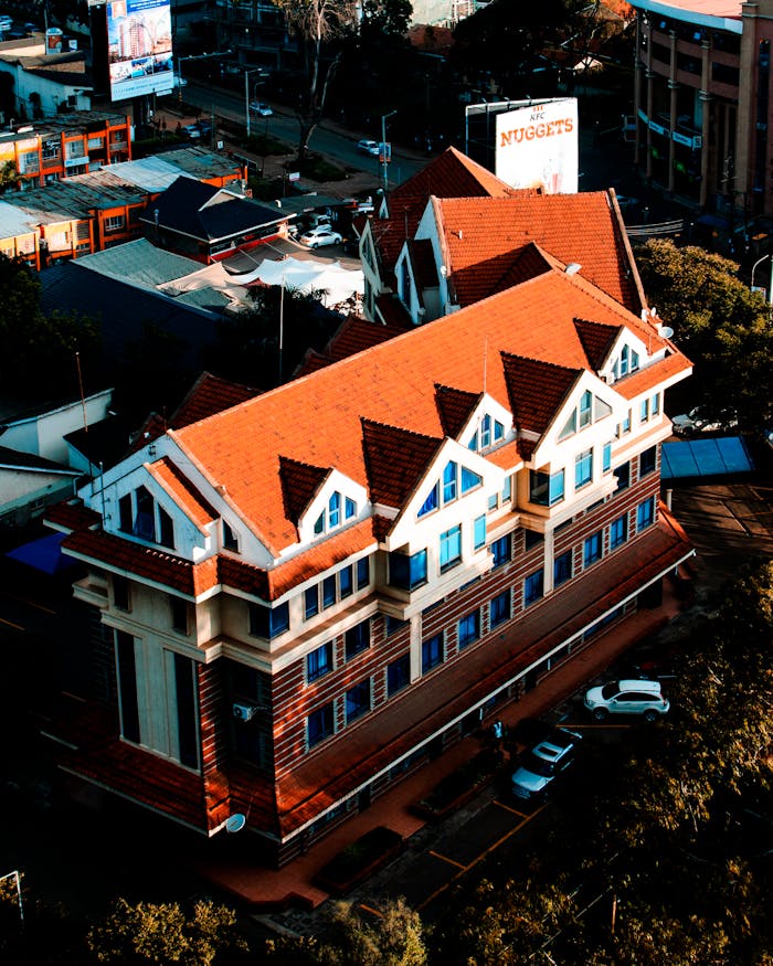 Aerial view of a unique urban building with a striking red roof and surrounding cityscape.