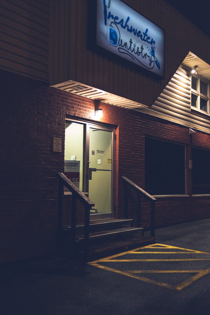 A nighttime view of an illuminated dental clinic entrance featuring a glowing signage and brick facade.